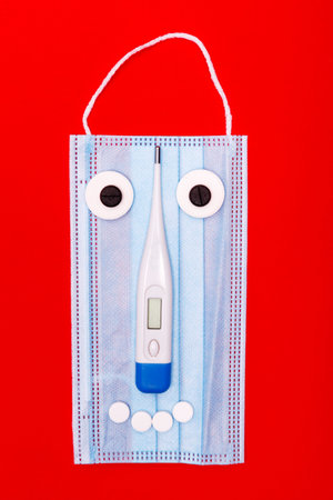 medical mask with a face of tablets and a thermometer on a red background