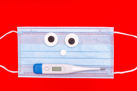medical mask with a face of tablets and a thermometer on a red background