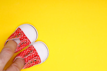 male hand with baby shoes in red with white polka dotsの写真素材