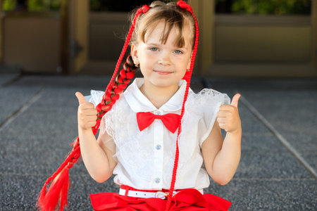 beautiful little girl with red pigtails and bow tie. the child shows thumbs up