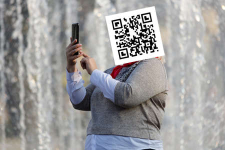 qr code on the face of a person holding a phone in his handの写真素材