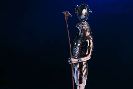 metal statue of the Egyptian god Ra with the head of a falcon on a black background with blue illuminationの写真素材