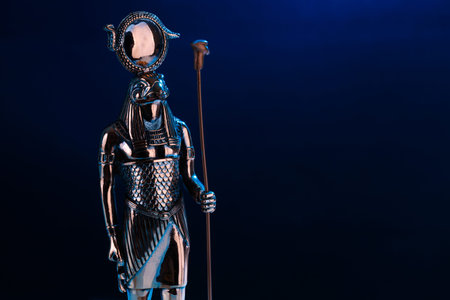 metal statue of the Egyptian god Ra with the head of a falcon on a black background with blue...