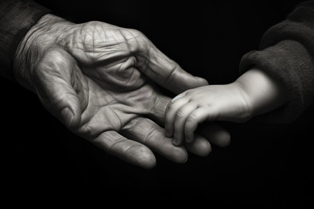 A touching black and white photo capturing the hand of a person gently holding a baby's hand. Perfect for illustrating the bond between a caregiver and a child. .の素材