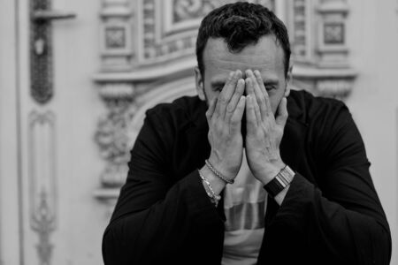 brunette man sitting and praying outdoors close-up in a jacketの写真素材