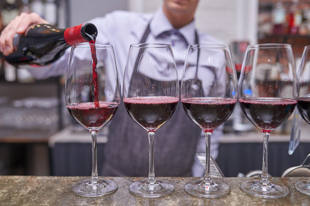 Bartender pours red wine into wine glasses from a bottle