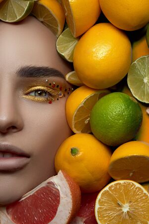 beautiful fashion professional model with bright makeup on a bright photo is lying with his mouth open on a background of fruit, lemon and lime citrus. High End retouch. Close up portraitの写真素材