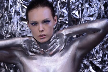 Closeup portrait of a young cute girl over grey background. Perfect bright makeup. Silver lips and eyebrows. Brunette with curly hair. Snow queen. White swan with plumage. Eye and lips.の写真素材