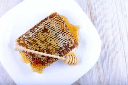 stick for honey near the honeycomb on a wooden background