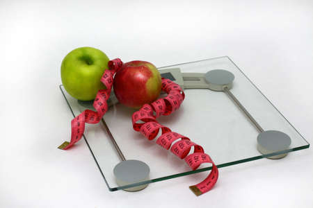 Two fresh apples green and red with pink measuring ribbon lie on glass floor scales white backgroundの写真素材