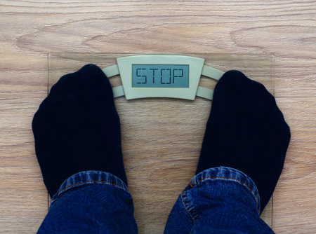 Man standing on weight scales with stop inscription. Concept of fat shaming.