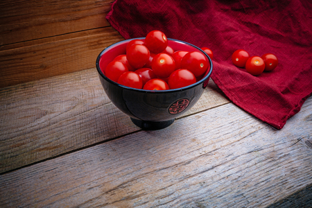 cherry tomatoes in a black and red pial on a wooden table with a red linen napkinの写真素材