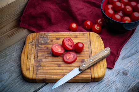cherry tomatoes in a black and red pial on a wooden table with a red linen napkin and kitchen knife...