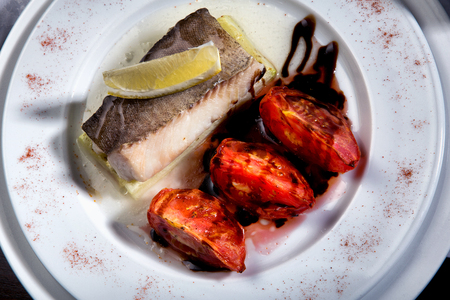 cod grilled with vegetables in wihte plate with tomatoes and lemonの写真素材