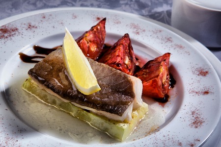 cod grilled with vegetables in wihte plate with tomatoes and lemonの写真素材