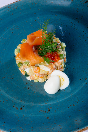 Russian salad on a blue plate with salmon and eggsの写真素材