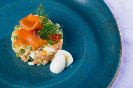 Russian salad on a blue plate with salmon and eggsの写真素材
