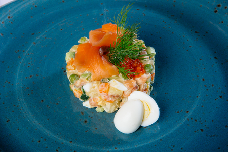 Russian salad on a blue plate with salmon and eggsの写真素材
