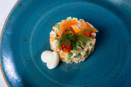 Russian salad on a blue plate with salmon and eggsの写真素材