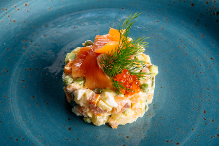 Russian salad on a blue plate with salmon and eggsの写真素材