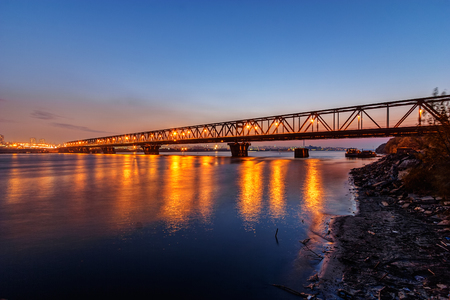 Steel bridge across river at night with artificial lightningの写真素材