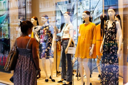 Woman is watching boutique window with mannequins in summer clothing