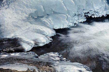 View of ice on the banks of small mountain creek with water in motionの写真素材
