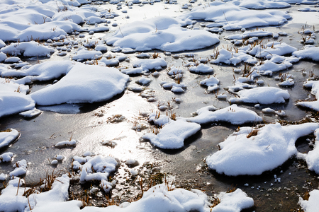 Puddles of melting snow on the field on sunsetの写真素材