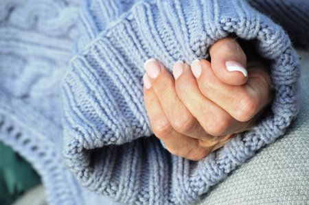 Hands of elderly woman in warm sweater, closeup of photoの写真素材