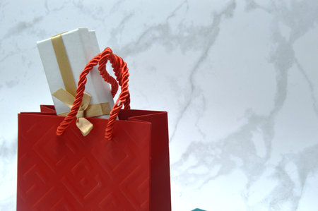Red paper bag with gift box on white marble background with copy spaceの写真素材