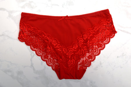 Red lace panties on white marble background, top view. female underwear