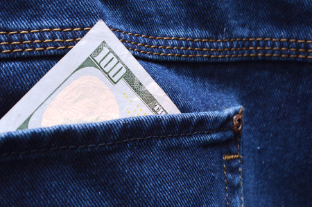 One hundred dollar bill sticking out of jeans pocket. close up.