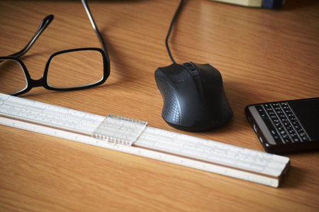 Computer mouse, glasses and a ruler on a wooden table in the officeの写真素材