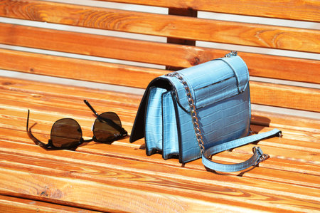 Blue handbag and sunglasses on a wooden bench in the park.の写真素材