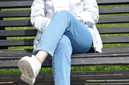 Young woman sitting on a bench in a park wearing jeans and sneakers