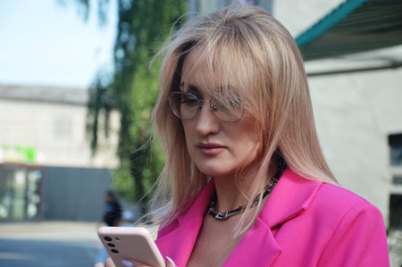 Portrait of a beautiful young woman in a pink jacket and glasses on the streetの写真素材