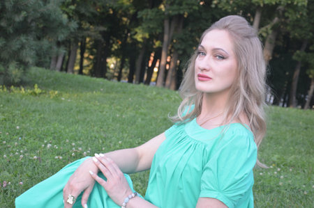 Beautiful girl in a green dress sitting on the grass in the parkの写真素材