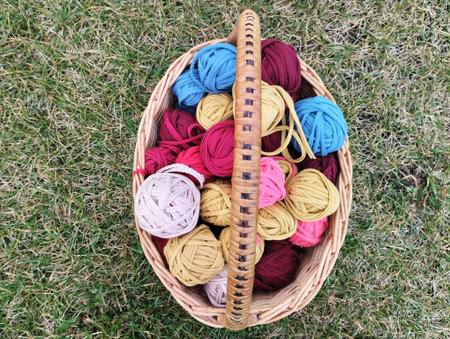 Basket of woolen threads for knitting on green grass background.