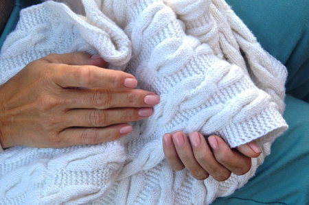 Female hands with beautiful manicure holding a white knitted sweater.の写真素材