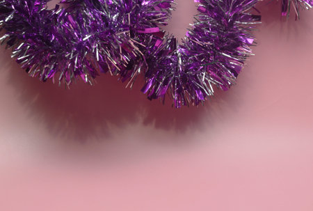 Purple Christmas tinsel on pink background with copy space for text