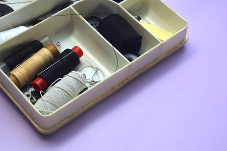 Sewing accessories in a box on a lilac background.