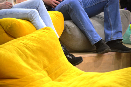 Couple sitting on yellow sofa, close-up of legs.の写真素材
