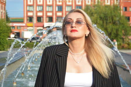 Portrait of a beautiful blonde girl in a jacket and sunglasses on the background of a fountainの写真素材