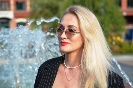 Portrait of a beautiful blonde woman in sunglasses on the background of a fountainの写真素材