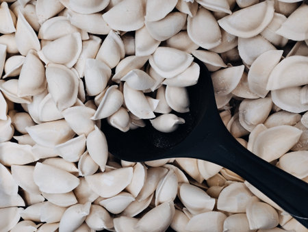 Close up of raw pelmeni with black spoon on white background