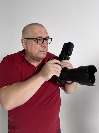 Senior photographer with a camera in his hands on a gray background.