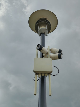 Security camera on blue pole with cloudy sky background, security concept.