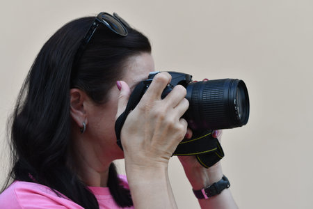 Female photographer taking pictures with a DSLR camera on a neutral background