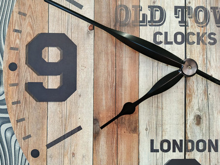 Close up of clock face showing 9 o'clock on wooden background