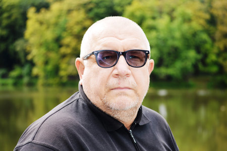 Portrait of a bald man in sunglasses against the background of the lake
